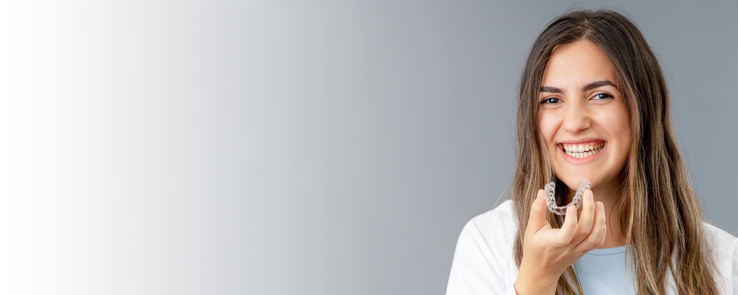 Woman smiling with hand near face against gray background in dental office setting