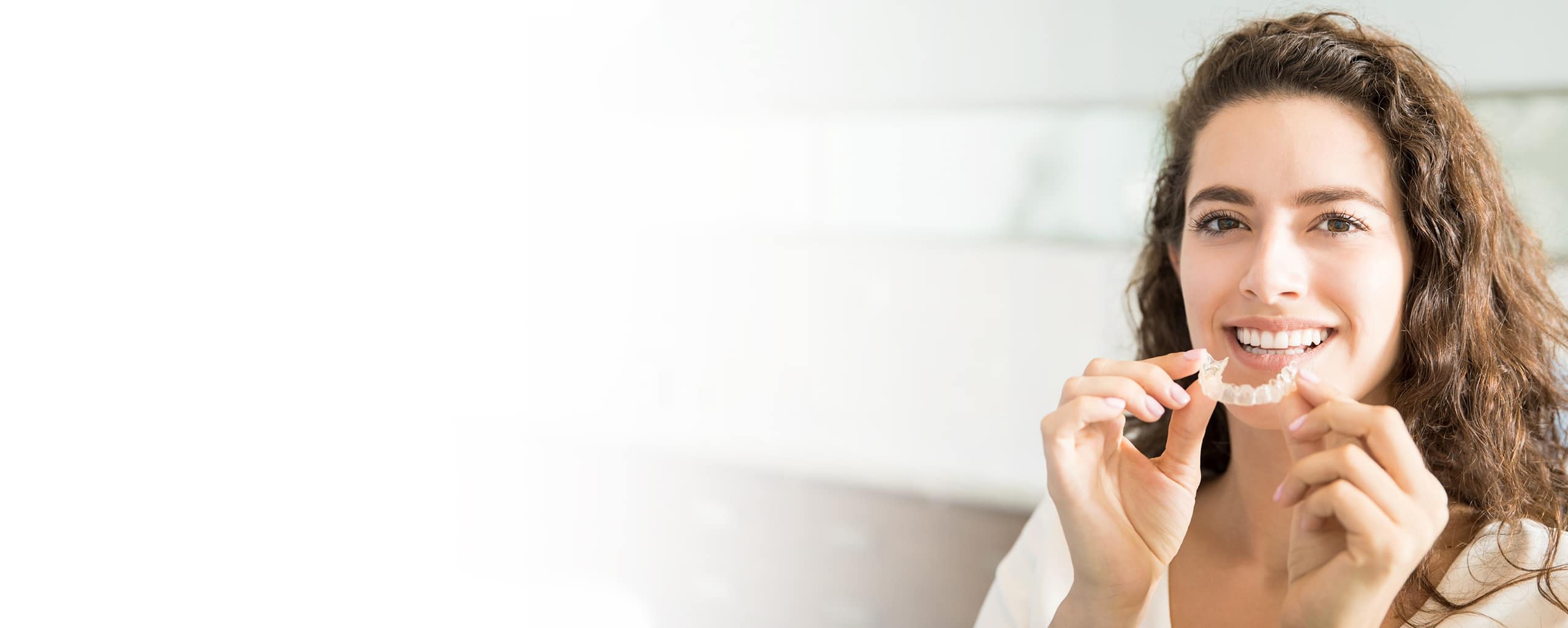 Woman flossing teeth in bright bathroom setting, smiling at camera