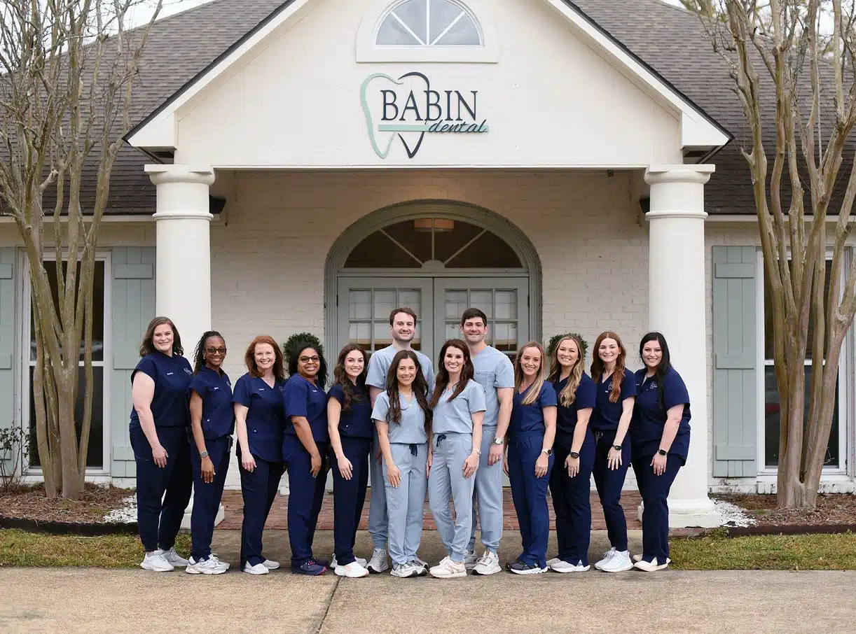 Babin Dental team posing together outside white dental office building with columns.