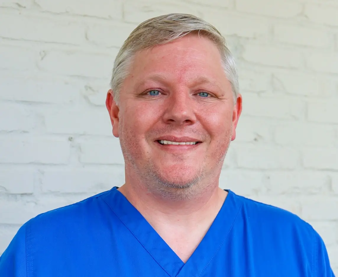 Professional male dentist in blue scrubs smiling at Baton Rouge dental practice.