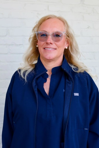 Professional headshot of Jennifer smiling while wearing glasses and dark blue scrubs.